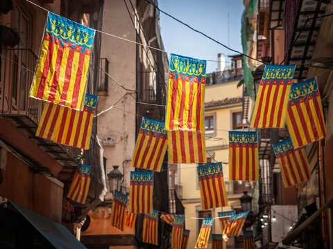 Strings of Comunitat Valenciana, or comunidad valenciana flags, called Senyera Valenciana hanging across a street in central Valencia, with old buildings in the background during a festive decoration.