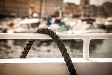 Thick three-strand mooring line draped over a white rail in a marina. The rope forms a loop against a blurred harbor, illustrating dock line use for securing boats to quays and piers. © Jerome