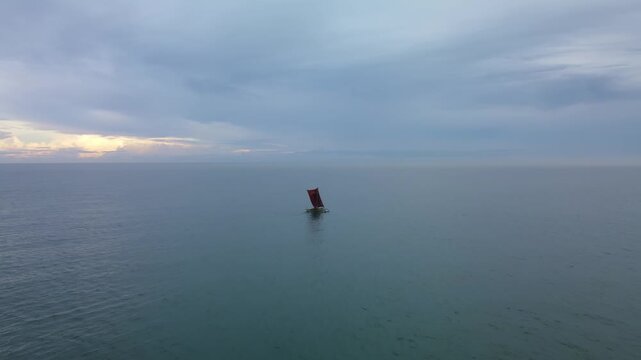 Traditional sri lankan fishing boat sailing under sail at sunrise in negombo, indian ocean. Early morning seascape with wooden outrigger canoe and fisherman silhouette gliding across calm ocean water.