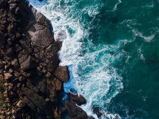 Aerial drone photo of ocean waves crashing against rocky shoreline. Dynamic naturel seascape with textured water,foam patterns and coastal rock viewed from above. minimalist and abstract.