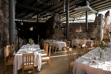 Rustic wedding reception setup inside a historic stone barn with elegant table settings, wooden chairs, soft natural light and minimalist floral centerpieces, creating an intimate countryside celebrat © Nele