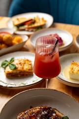 A vibrant glass of refreshing drink stands out among an array of beautifully plated dishes, highlighting the joy of sharing flavorful meals with friends in a warm atmosphere