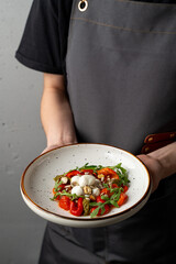 A talented chef showcases a beautifully arranged plate of colorful vegetables, topped with herbs and garlic, in a modern kitchen setting