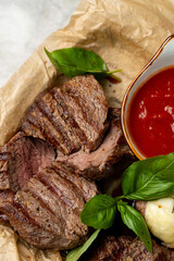 Tender slices of grilled steak are beautifully arranged with vibrant green basil. A small bowl of rich tomato sauce adds a burst of color and flavor to this mouthwatering dish