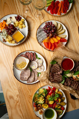 At a wooden table, a colorful spread of gourmet cheeses, fresh fruits, roasted meats, and assorted veggies awaits, perfect for sharing and enjoying together