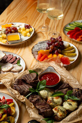 Delight in a colorful array of grilled meats, fresh fruits, and savory cheeses displayed on a rustic wooden table. Glasses of wine add to the inviting ambiance of this joyful gathering