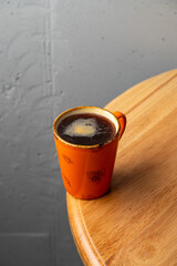 Rich, dark coffee fills a vibrant orange cup, contrasting beautifully with the warm tones of a polished wooden table. The atmosphere feels inviting and intimate
