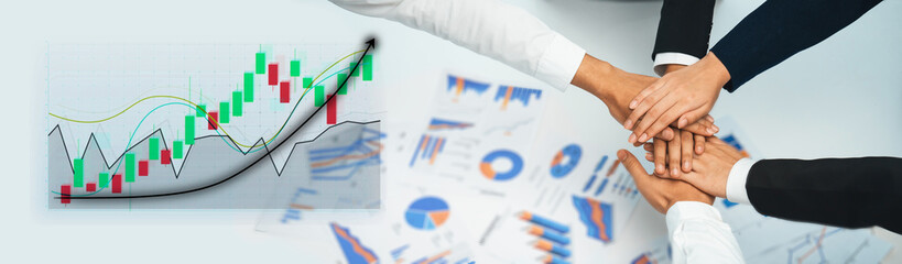Diverse business team united in success with hands together over financial graphs showing positive...