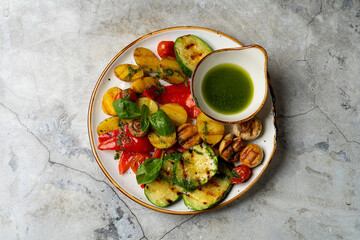 Colorful grilled vegetables arranged beautifully on a rustic plate, accompanied by a small bowl of fragrant green dressing. Perfect for a summer meal