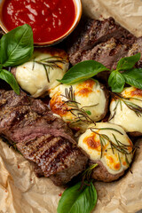Sizzling grilled steak sits alongside creamy cheese, drizzled with olive oil and garnished with fresh herbs. A bowl of rich tomato sauce adds a touch of flavor, perfect for dipping