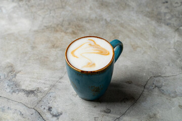 A beautiful turquoise mug holds a perfectly crafted latte with intricate swirls of creamy milk and coffee. The stone surface enhances the warm tones of the drink, creating a cozy vibe