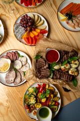 Tasty assortment of grilled meats and vibrant veggies garnished with fresh basil, surrounded by plates of colorful fruits, perfect for a joyful gathering