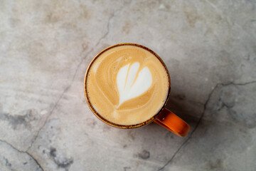 Warm latte with beautiful leaf-shaped art sits gracefully on a textured stone surface, embodying the cozy charm of a coffee shop afternoon