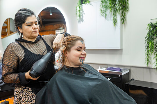 Hairdresser drying client hair in beauty salon with moko kauae