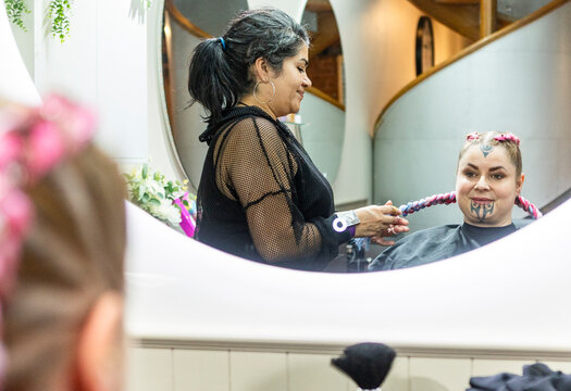 Hairdresser braiding colorful hair extensions in a New Zealand salon