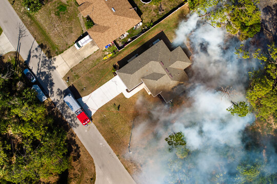 Vegetation fire burns jungle forest near Florida houses as firefighters and fire trucks work to contain flames threatening nearby neighborhoods