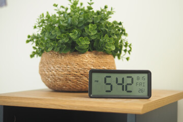 Clock shows time on table with plant in background