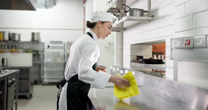 Chef, cleaning and woman with cloth, kitchen and sanitation with chemical or maintenance of surface. Wiping, workstation and person with spray for disinfection, hygiene and food safety in restaurant