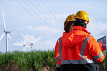 Over-the-shoulder view of two engineers in hard hats and safety gear during a sunset briefing. Professional technical team discussing maintenance strategy at a green energy wind farm.