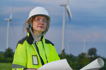 Portrait of a female engineer in a white hard hat and high-visibility jacket holding plans at a...