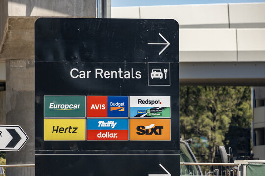 Directional car rental signage at Melbourne airport, Australia, displaying major rental brands including Europcar, Avis, Budget, Redspot, Hertz, Thrifty, Dollar, and SIXT. 