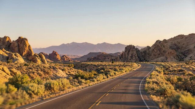 A scenic asphalt road winds through an arid desert landscape during golden hour. Distant mountains are visible under a clear sky. The scene is bathed