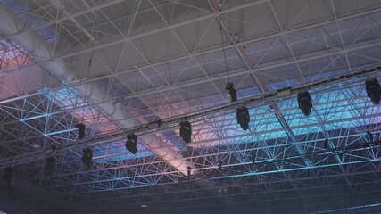 overhead view of metal roof trusses and suspended stage lighting inside large venue