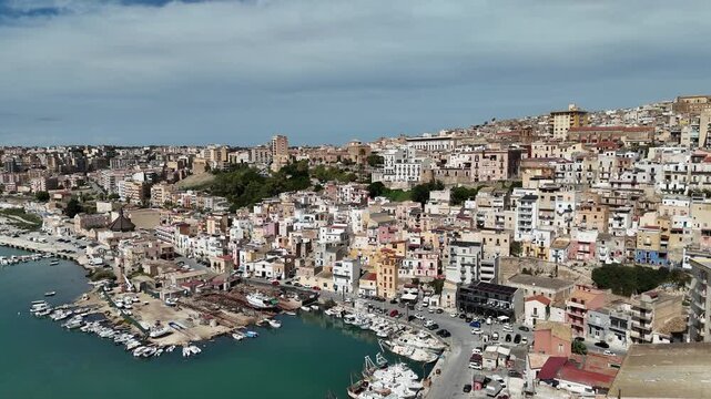 Aerial view of Sciacca revealing a dense hillside town, historic buildings, marina docks, and calm harbor waters along the southern Sicilian coast.