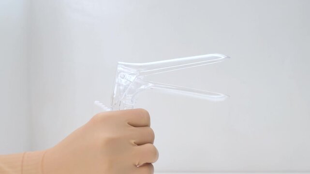Doctor's hand in a medical glove opening a disposable plastic vaginal speculum