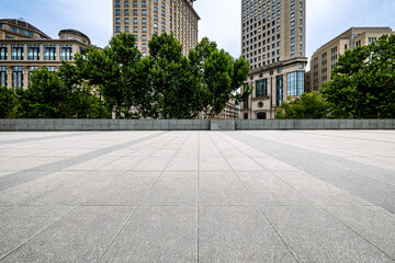 Empty square floor in a modern urban area with commercial buildings and green trees. © zhao dongfang