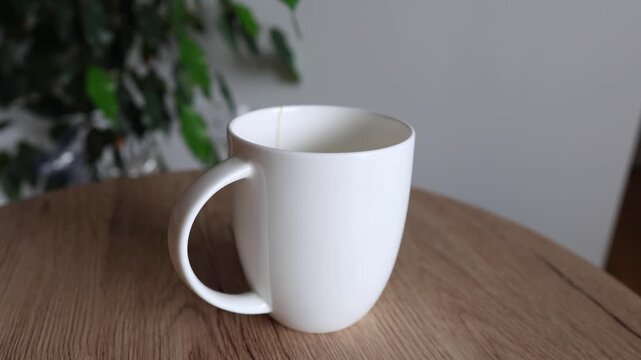 Close-up of a hand placing a teabag into a white ceramic cup on a wooden table. Minimalist, calm routine concept with soft natural light. Simple everyday moment, tea preparation at home.