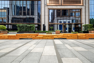 Modern building facade with glass reflections and an empty tiled plaza.