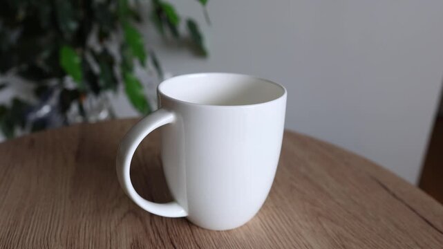 Close-up video of a hand removing a teabag from a white ceramic cup on a wooden table, simple home routine.