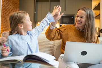 Mother and daughter giving high five, enjoying learning and studying at home
