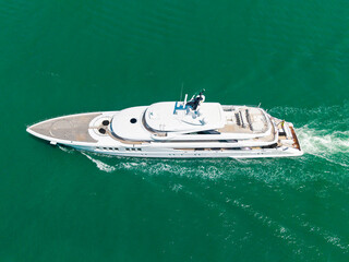 Top view of a luxury yacht sailing along the Miami coast. Aerial shot of a white yacht in turquoise tropical waters. Elite yacht. Top drone angle showing yachts in a vibrant marina. Luxury yachts