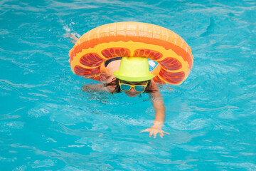Child in swimming pool on inflatable float ring. Water toy, healthy outdoor sport activity for children. Kids beach fun. Child splashing in summer water pool.