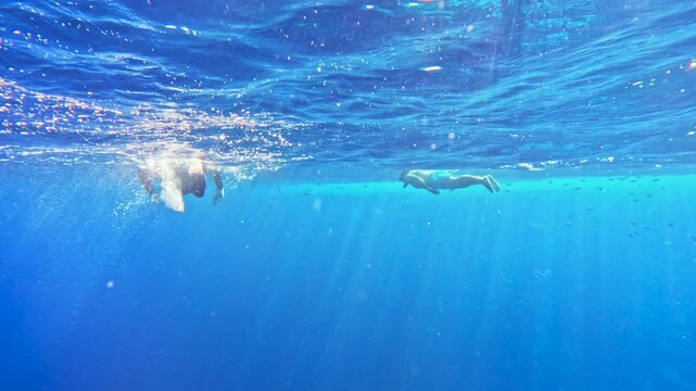 Snorkeling tourists swimming on water surface above blue abyss in clear deep sea