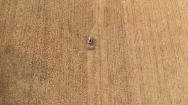 High-angle drone shot of a crawler tractor working a large cultivated field in rural Italy, smoothing dry soil into neat parallel lines on gently rolling hills.