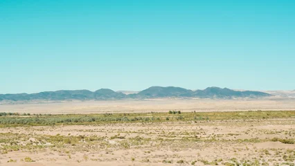 Selbstklebende Fototapeten Türkis A wide panoramic view of a dry desert landscape with distant mountains under a blue sky  © HABI ANGGARA PUTRA