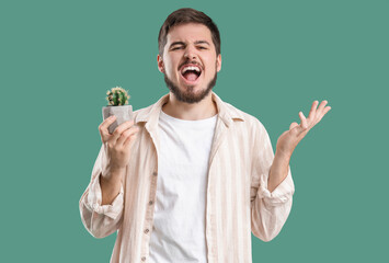 Young man with hemorrhoids and cactus screaming on green background