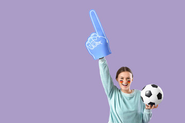 Female German soccer fan with ball and foam hand on lilac background
