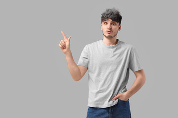 Shocked young man with graying hair pointing at something on light background