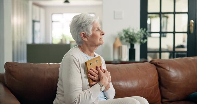 Sad, old woman and thinking with photo frame on sofa for loss, nostalgia or sorrow in retirement. Lonely widow, senior person with depression and hug picture in home for memory, broken heart or grief