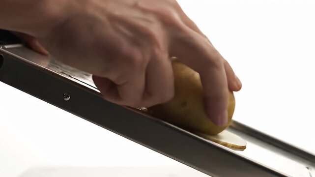 Hand slicing potato chips thin on a mandoline slicer for cooking preparation