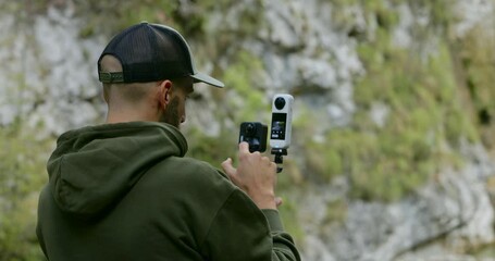 A man is holding two action cameras outdoors preparing to record content for social media.