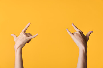 Two hands form a rock sign gesture against a vivid orange background, conveying energy, confidence,...
