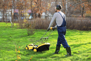 Male gardener using lawn mower outdoors, back view