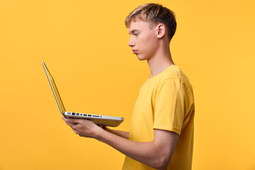 Young man using a laptop against a bright yellow background, showcasing technology, concentration...