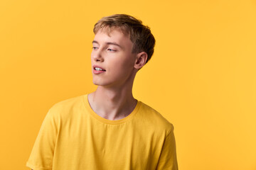 Young man in a bright yellow shirt against a solid yellow backdrop, looking away with a relaxed...