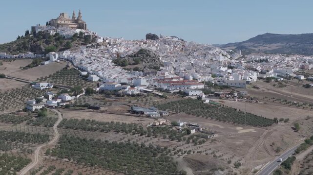 Aerial drone panorama of Olvera white hill town in Andalusia, Spain, with historic castle and church overlooking dense whitewashed village, olive groves, farmland and rural Mediterranean landscape